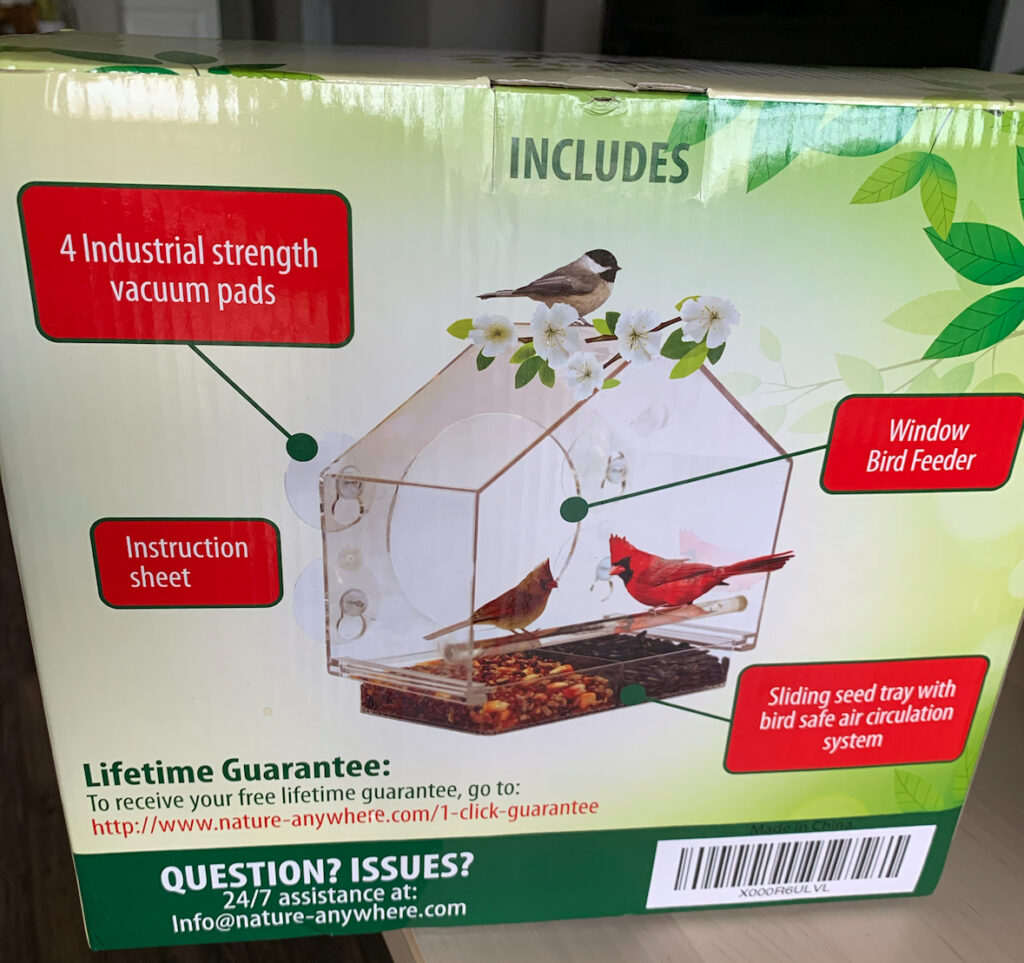 A bird feeder with suction cups that attaches to a window sitting it its box.