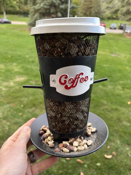 A bird feeder shaped like a coffee cup filled with peanuts. 