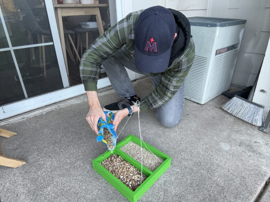 A tray bird feeder being filled with two types of bird seed on a patio.